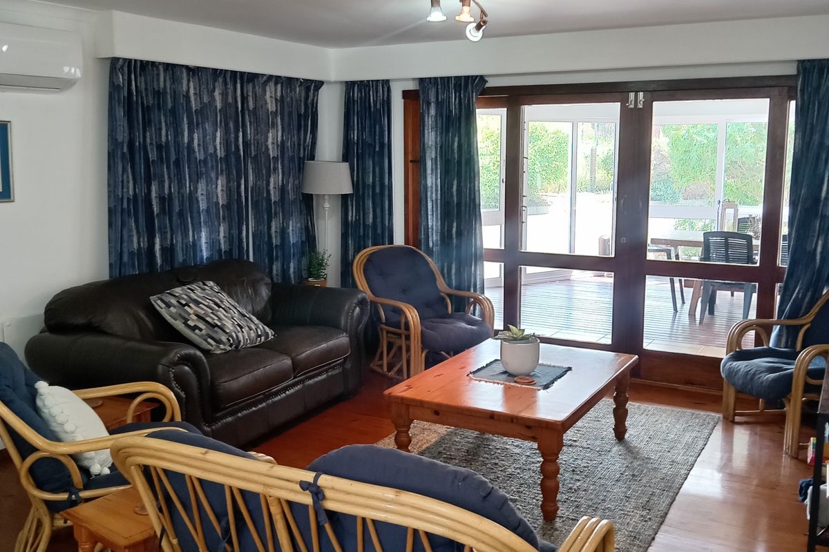 A comfortable living room featuring polished timber flooring, track lighting, and large glass sliding doors providing direct access to an outdoor patio area.