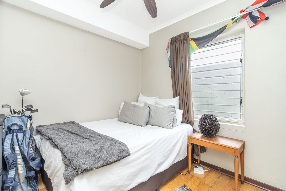 A cozy bedroom featuring timber flooring, a ceiling fan, and a louvered window providing natural light.