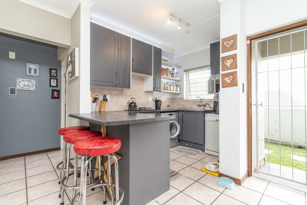 Compact kitchen featuring dark grey cabinetry, a breakfast bar, tiled flooring, and direct access to an outdoor area through a security gate.
