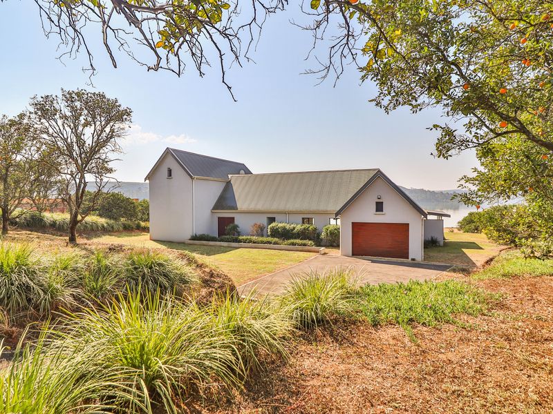 A well-maintained residential property featuring a metal roof, integrated garage, and a paved driveway, set within a spacious, landscaped garden environment.