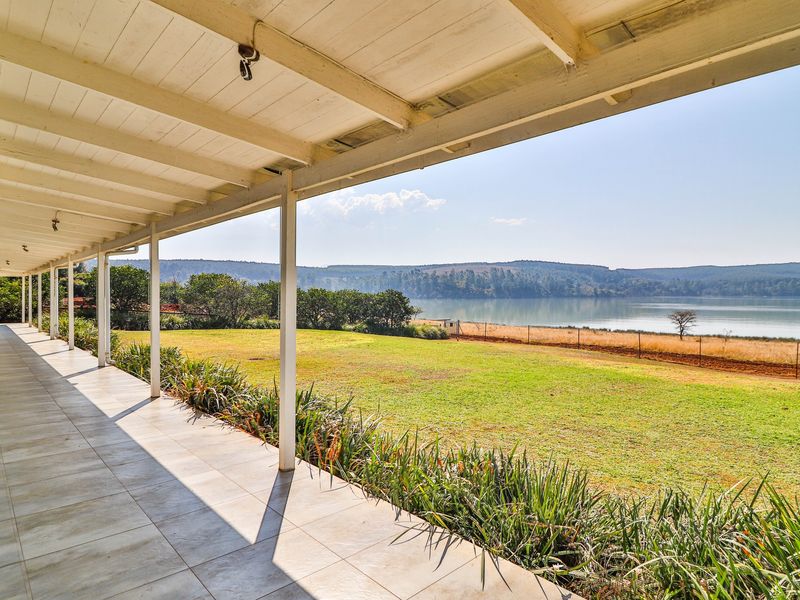 A spacious covered patio featuring tiled flooring and timber ceiling, offering expansive views over the garden and lake.