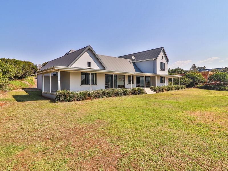 Rear view of a modern farmhouse-style home featuring a spacious covered veranda, metal roofing, and large sliding glass doors opening onto a landscaped garden.