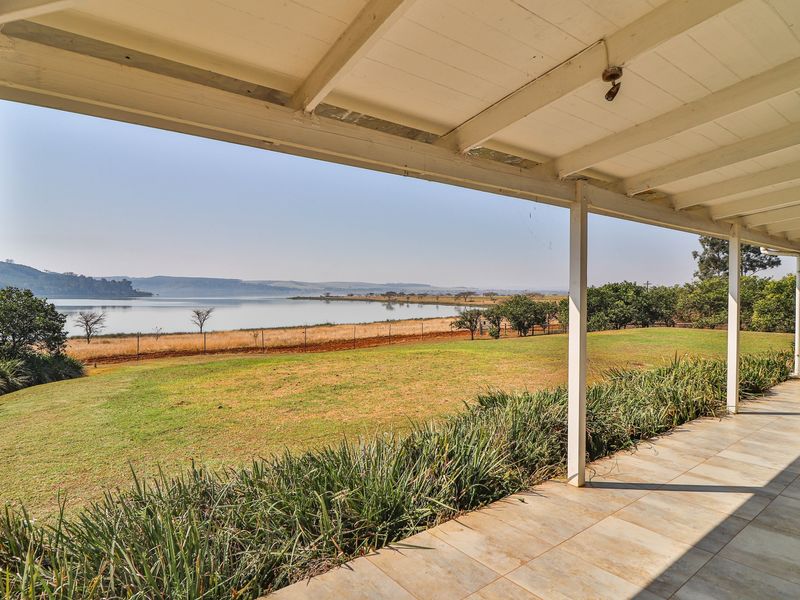 A spacious covered patio featuring tiled flooring and timber support posts, offering expansive views over the garden and lake.