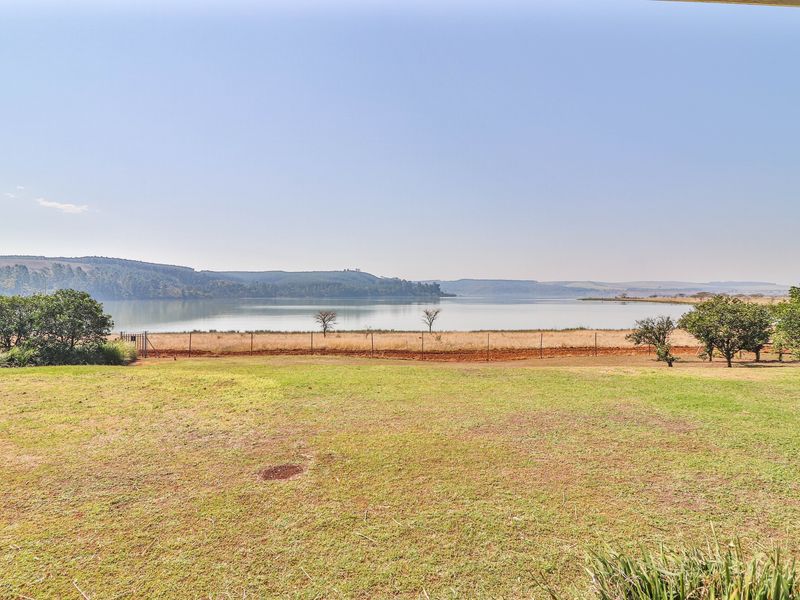 A scenic view overlooking a large dam or lake with surrounding hills and open grassy landscape.