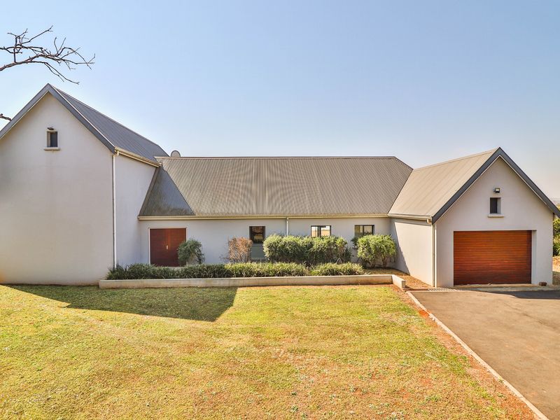 Front elevation of a modern farmhouse-style home featuring a corrugated metal roof, timber garage door, and a paved driveway with landscaped garden beds.
