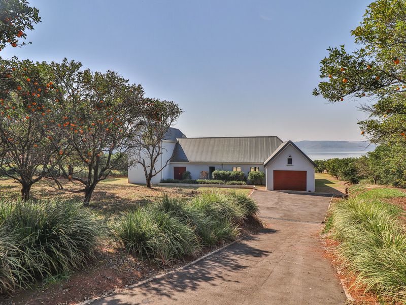 A well-maintained single-story residence featuring a metal roof, attached garage, and a paved driveway, set within a spacious garden with mature fruit trees.
