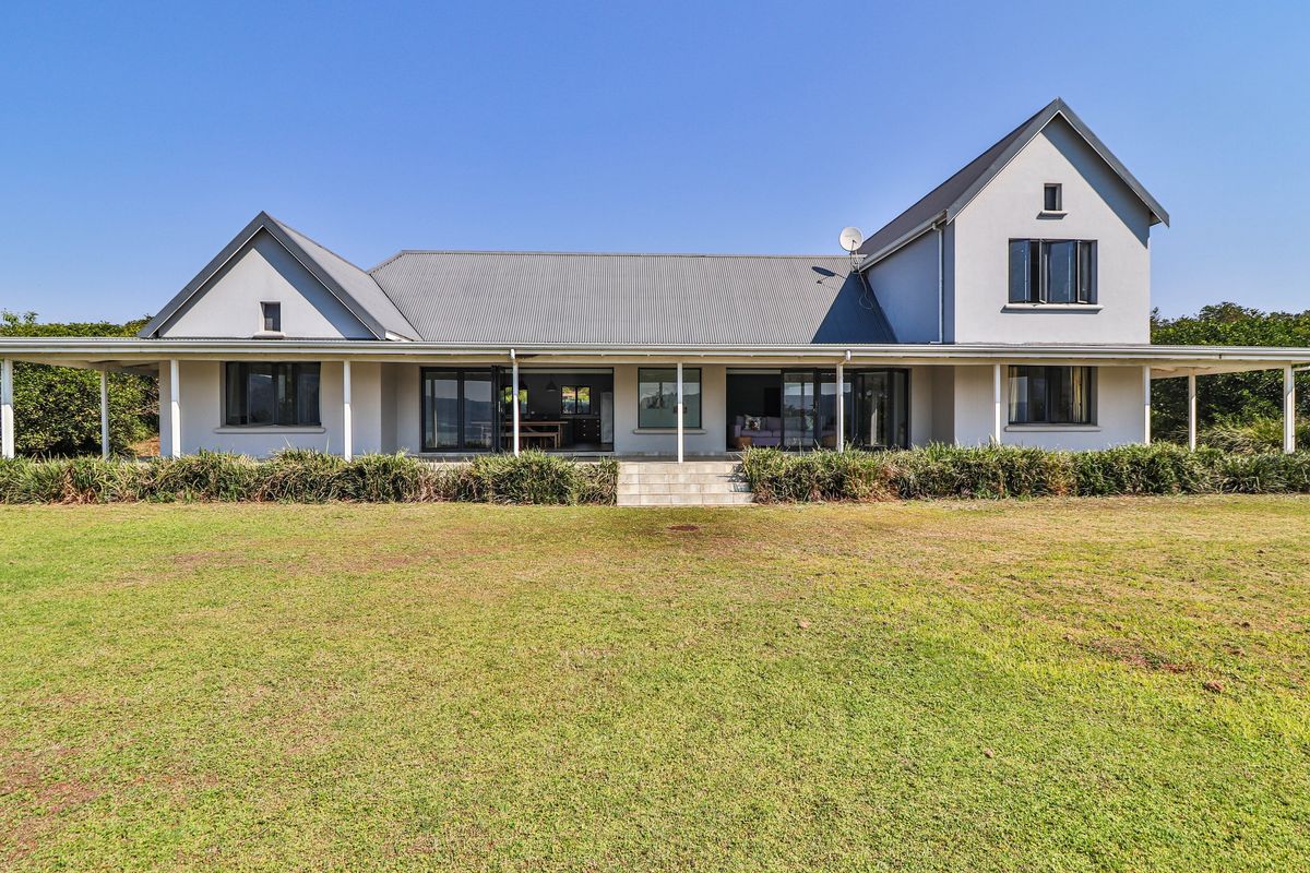 Rear view of a spacious two-story house featuring a large lawn, covered patio, and extensive sliding glass doors leading into the home.