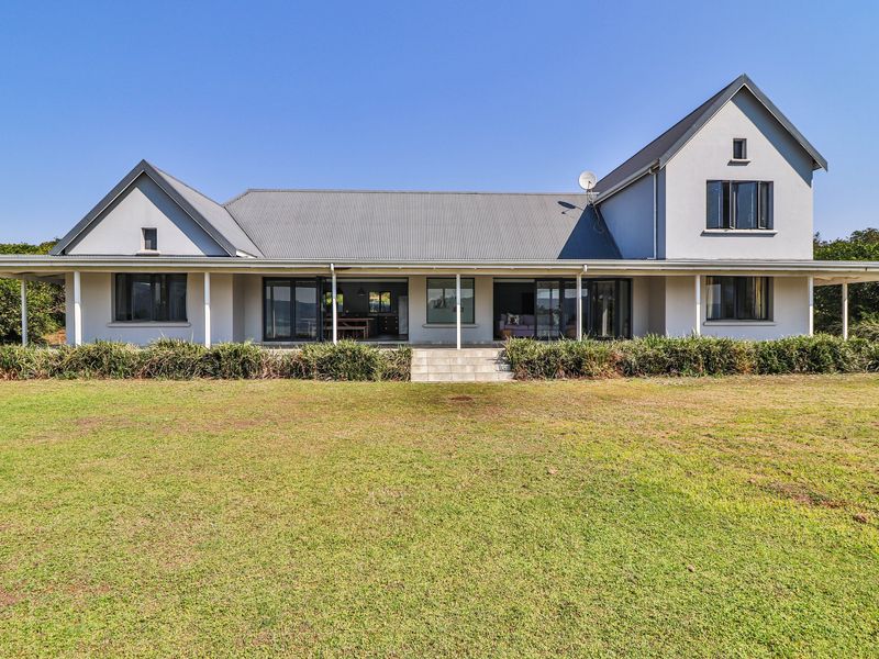 Rear view of a spacious two-story house featuring a large lawn, covered patio, and extensive sliding glass doors leading into the home.