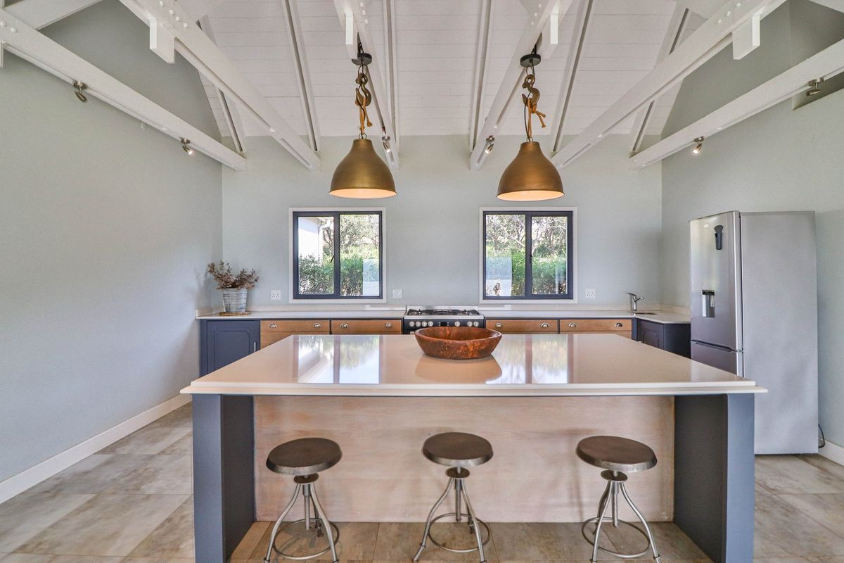 Modern kitchen featuring a large central island with stone countertop, exposed white timber beams, and high-quality cabinetry with integrated appliances.