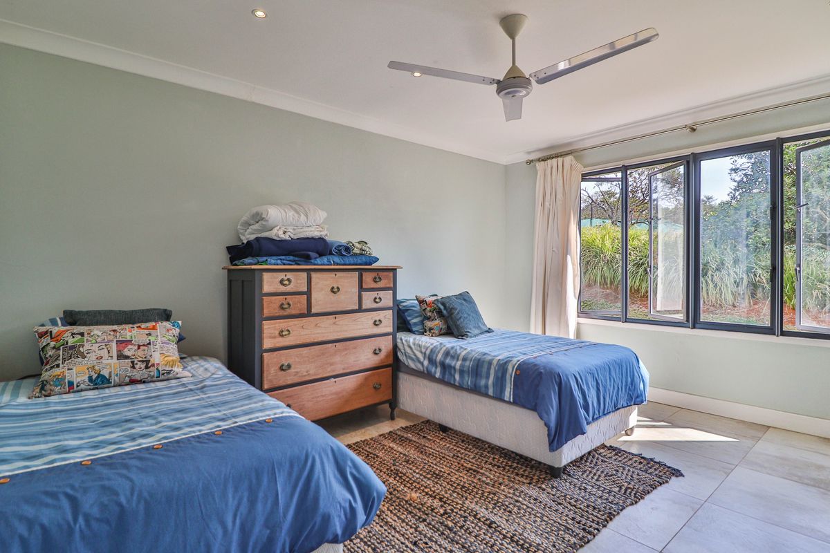 A well-lit bedroom featuring tiled flooring, a ceiling fan, and large casement windows providing natural light and garden views.