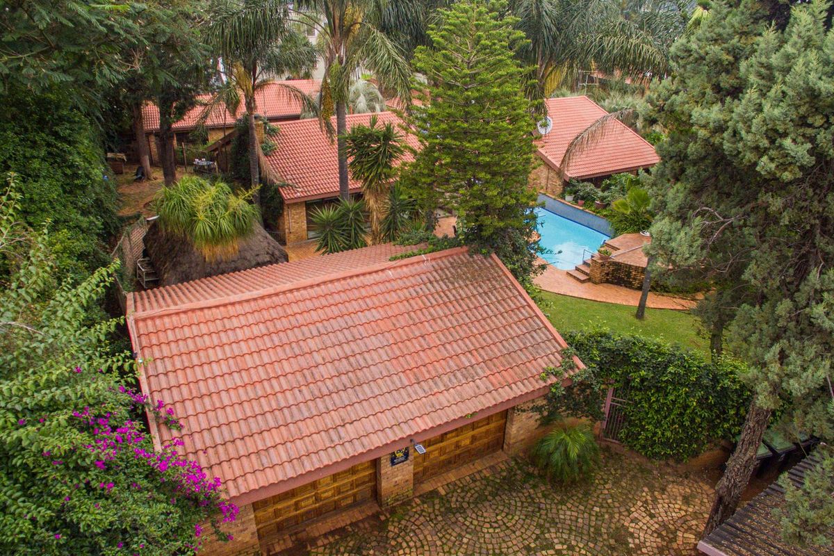 Aerial view of the property featuring a swimming pool, tiled roof structures, a garage, and established garden surroundings.