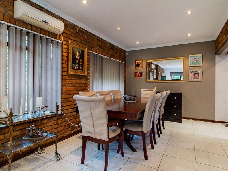 A well-maintained dining room featuring an exposed brick feature wall, tiled flooring, recessed lighting, and a wall-mounted air conditioning unit.