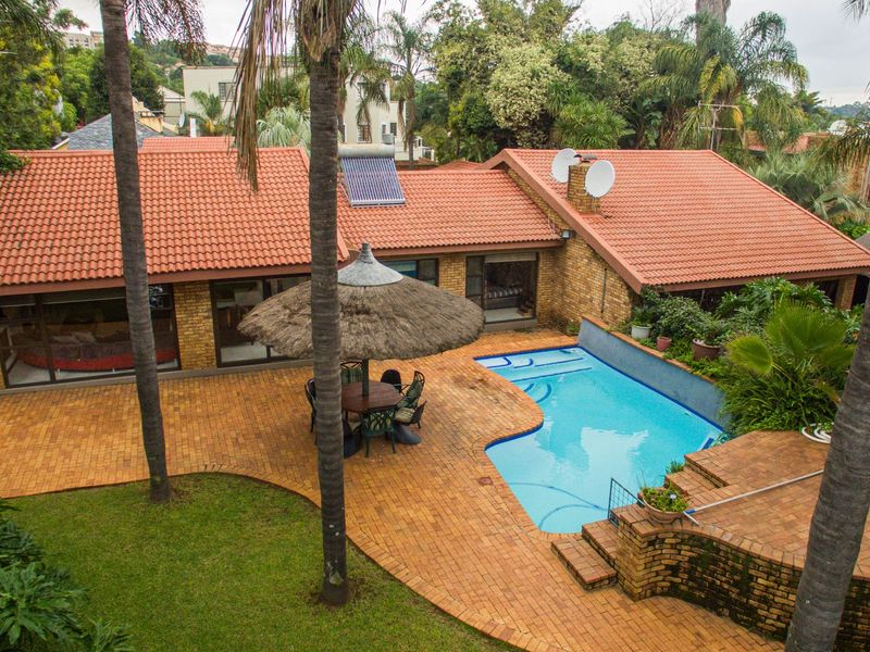 Aerial view of the rear exterior featuring a swimming pool, brick paved patio area, and a house with a terracotta tile roof.