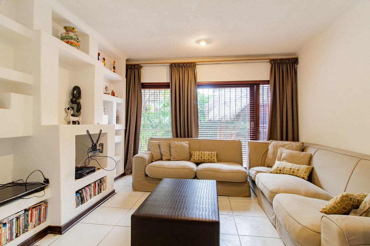 A comfortable living room featuring built-in shelving units, tiled flooring, and large sliding glass doors that provide natural light and garden access.