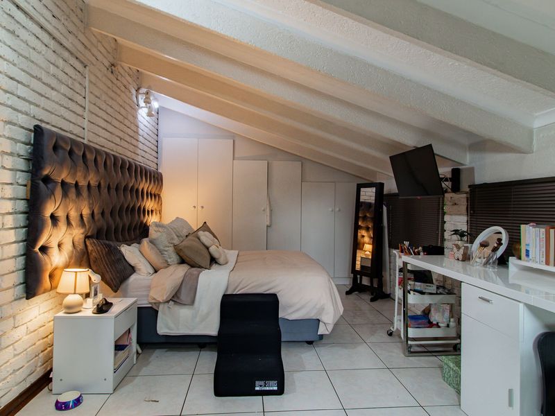 A spacious bedroom featuring exposed ceiling beams, white painted brick walls, built-in storage cupboards, and tiled flooring.
