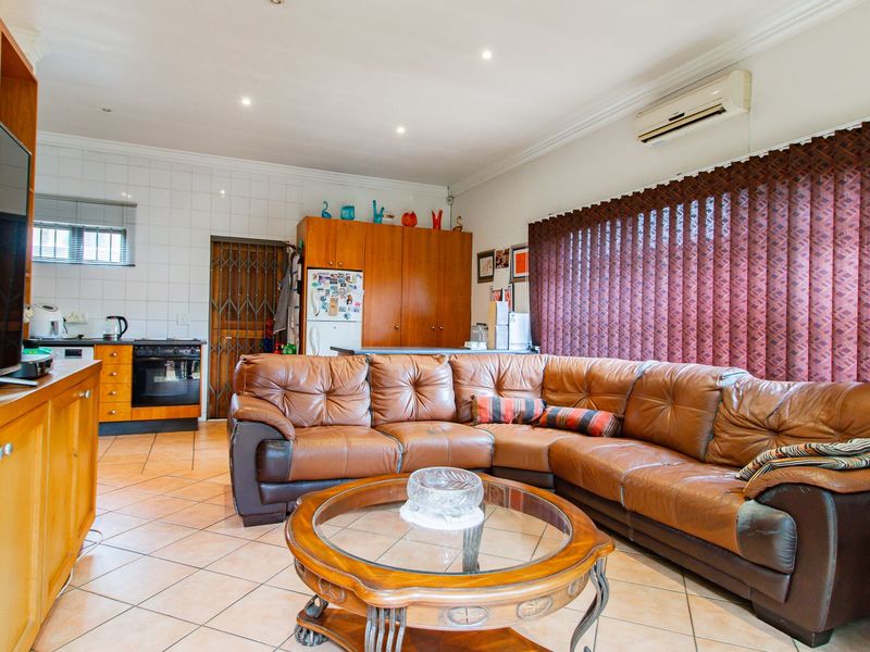 Open-plan living and kitchen area featuring tiled flooring, built-in cabinetry, integrated appliances, and a wall-mounted air conditioning unit.