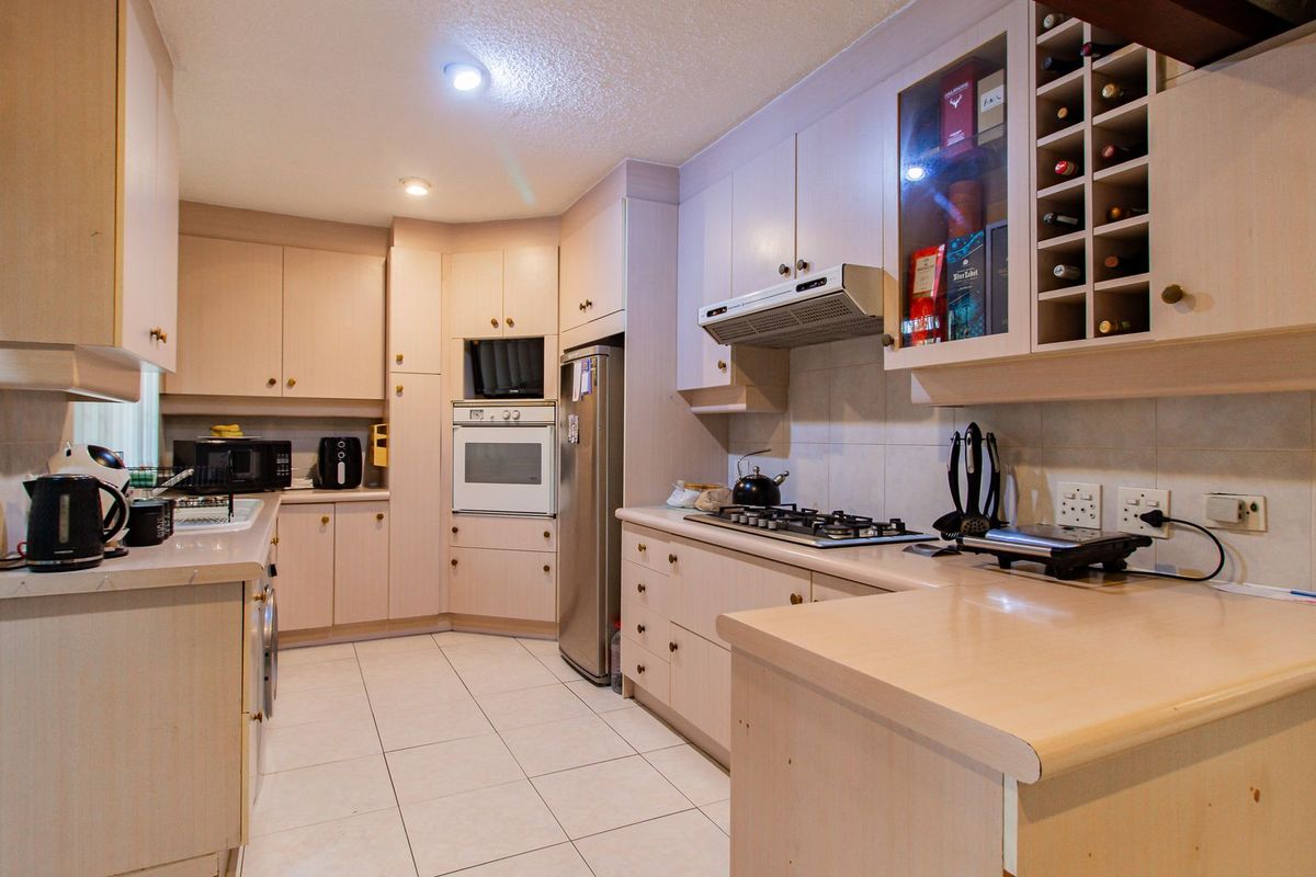 A functional kitchen featuring light-toned cabinetry, laminate countertops, built-in oven, gas hob, and integrated wine storage with tiled flooring and backsplash.