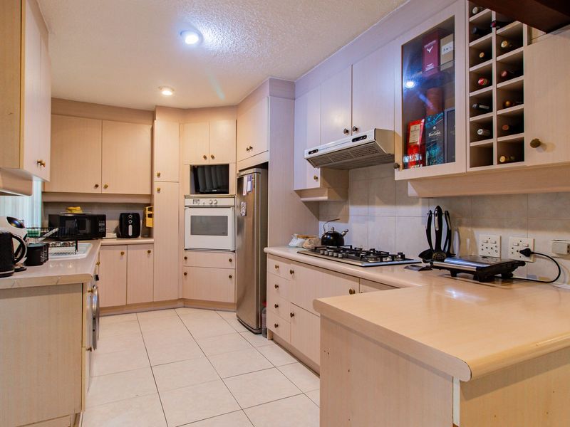 A functional kitchen featuring light-toned cabinetry, laminate countertops, built-in oven, gas hob, and integrated wine storage with tiled flooring and backsplash.