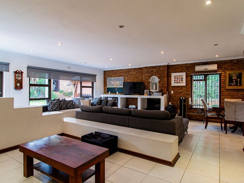 Spacious open-plan living area featuring an exposed brick wall, built-in concrete shelving, tiled floors, and recessed lighting with views to the garden.