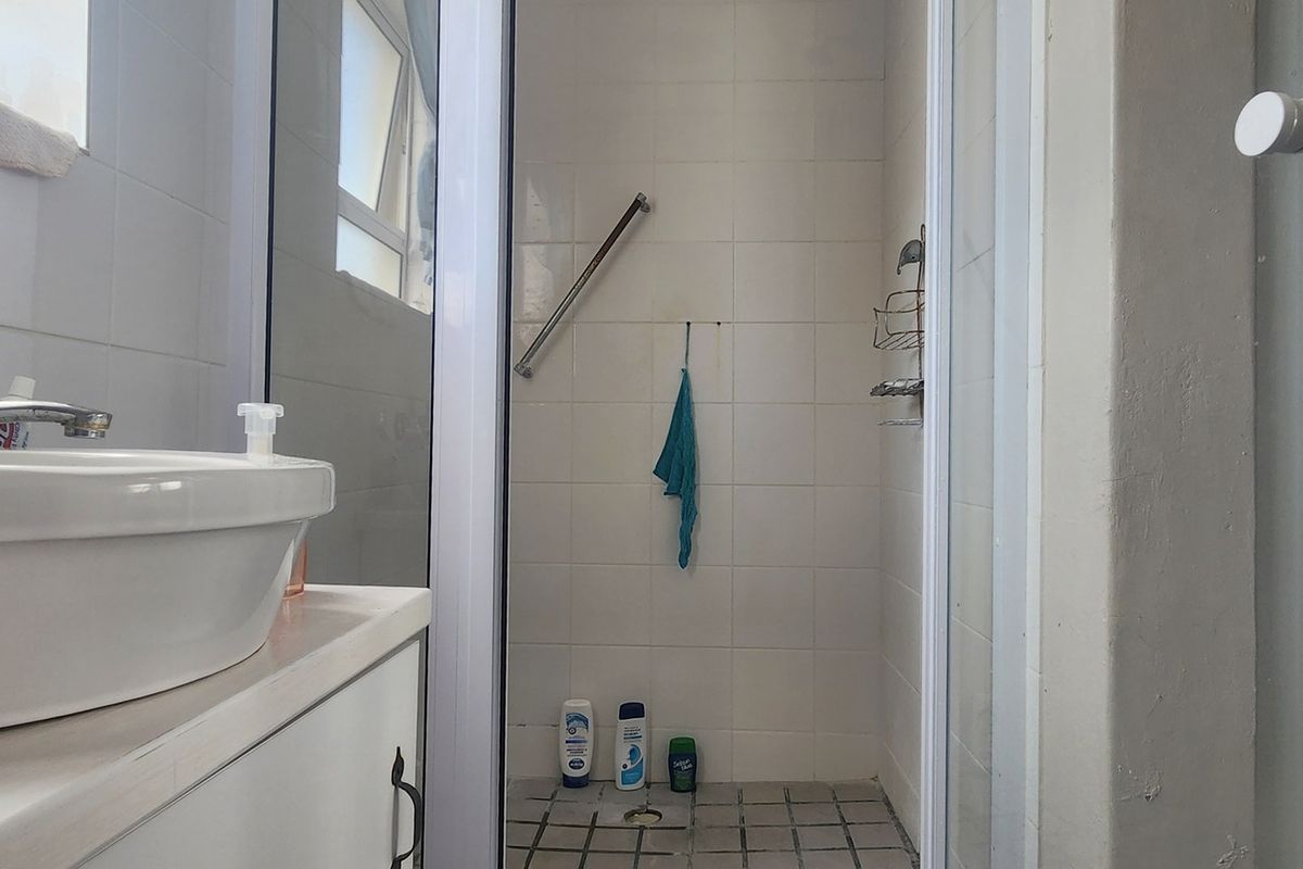 A functional bathroom featuring a vanity with a countertop basin and a separate shower enclosure with a grab rail and tiled finishes.
