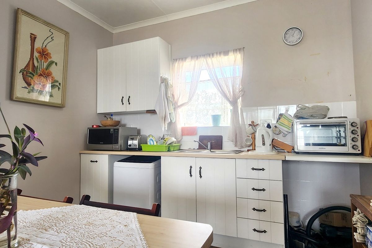 A functional kitchen featuring white cabinetry, a laminate countertop, and a tiled splashback, offering a practical layout for daily meal preparation.