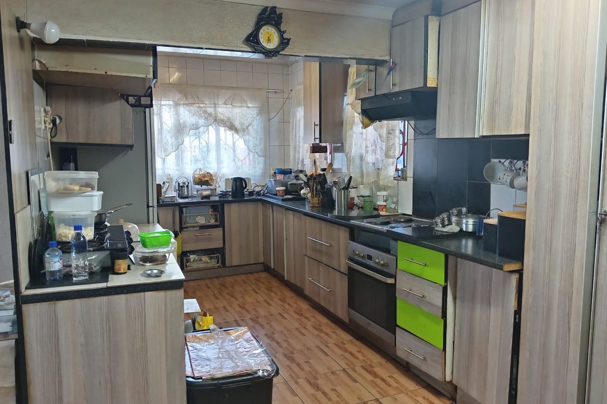 A functional kitchen featuring wood-look cabinetry, built-in oven, hob, and extractor fan with tiled flooring and a tiled backsplash.