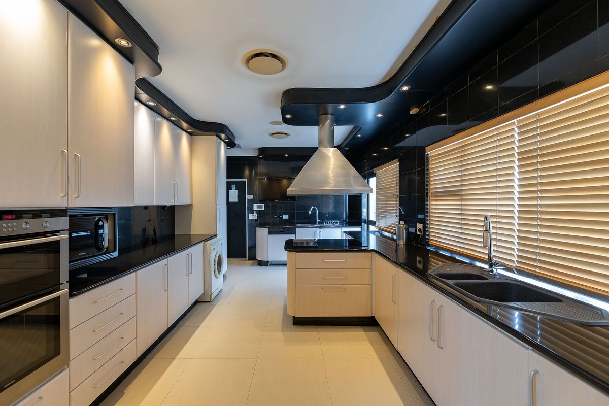 Modern kitchen featuring light wood cabinetry, contrasting black granite countertops, integrated appliances, and a central island with a stainless steel extractor fan.