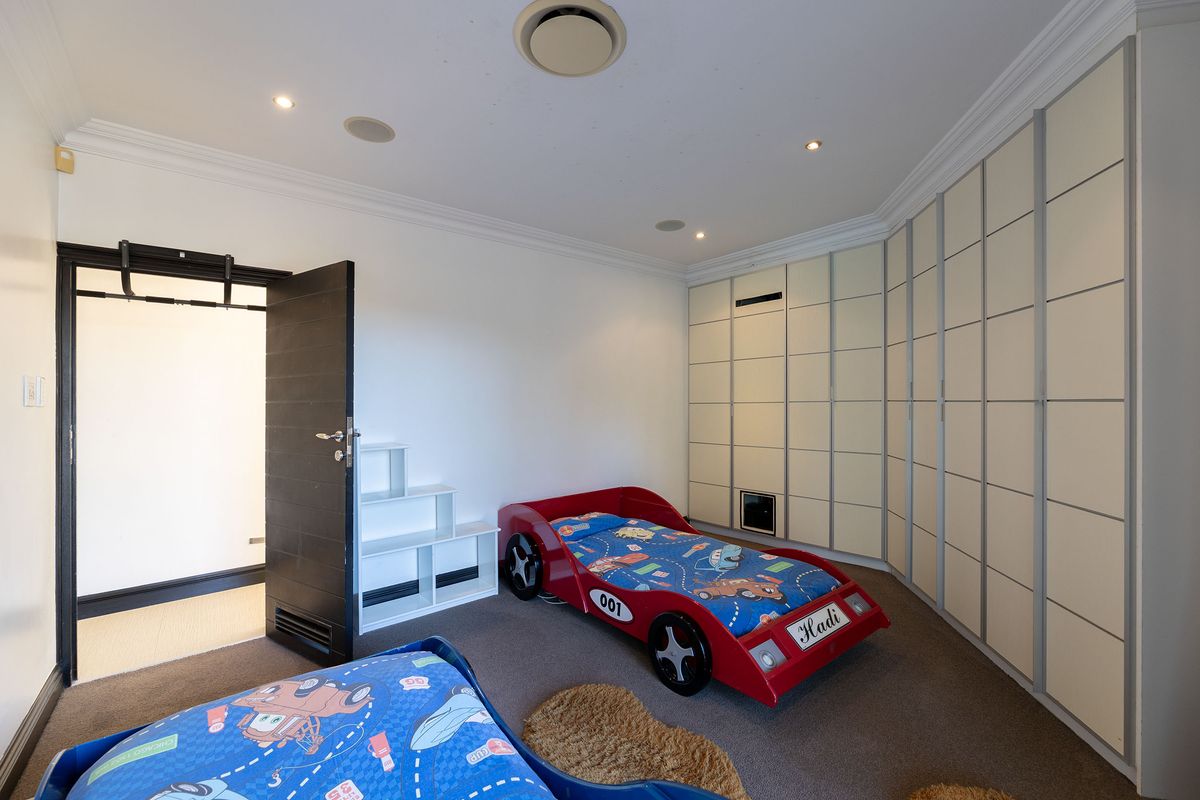 A spacious bedroom featuring extensive built-in cabinetry, recessed ceiling lighting, integrated speakers, and ducted air conditioning.