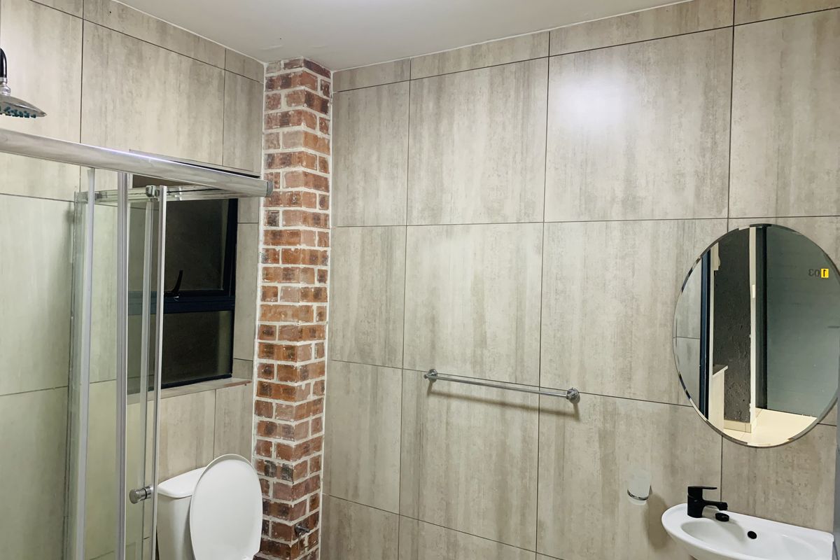 Modern bathroom featuring a shower enclosure, wall-mounted basin, and a distinctive exposed brick column accent wall with neutral ceramic tiling.