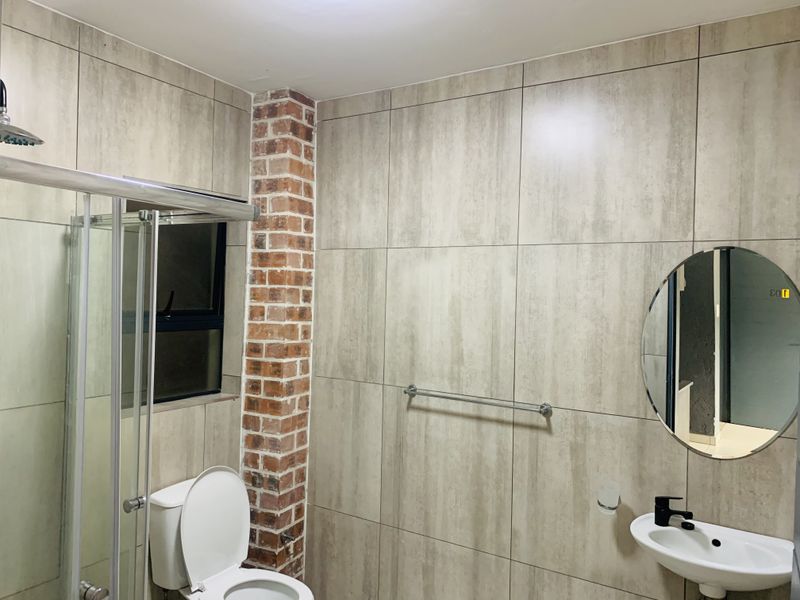 Modern bathroom featuring a shower enclosure, wall-mounted basin, and a distinctive exposed brick column accent wall with neutral ceramic tiling.
