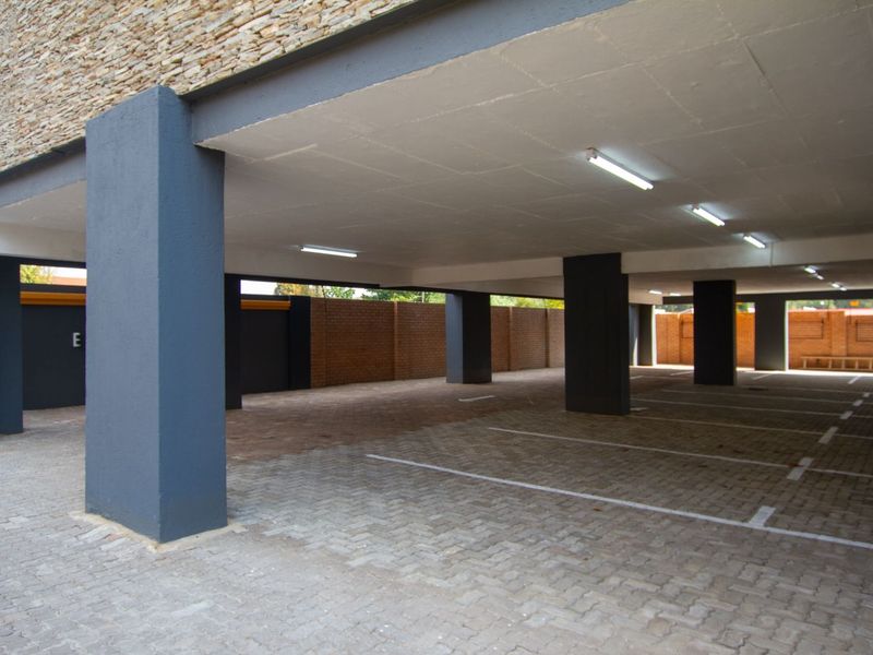 A clean, covered parking garage area featuring paved flooring, concrete structural pillars, and overhead fluorescent lighting.