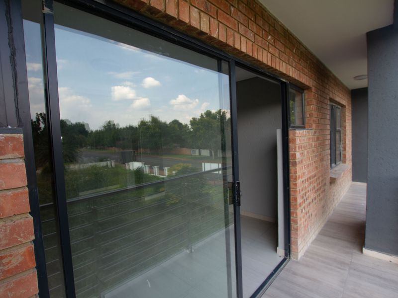A covered balcony featuring exposed brick walls, tiled flooring, and a metal balustrade, providing an outdoor extension to the apartment living space.