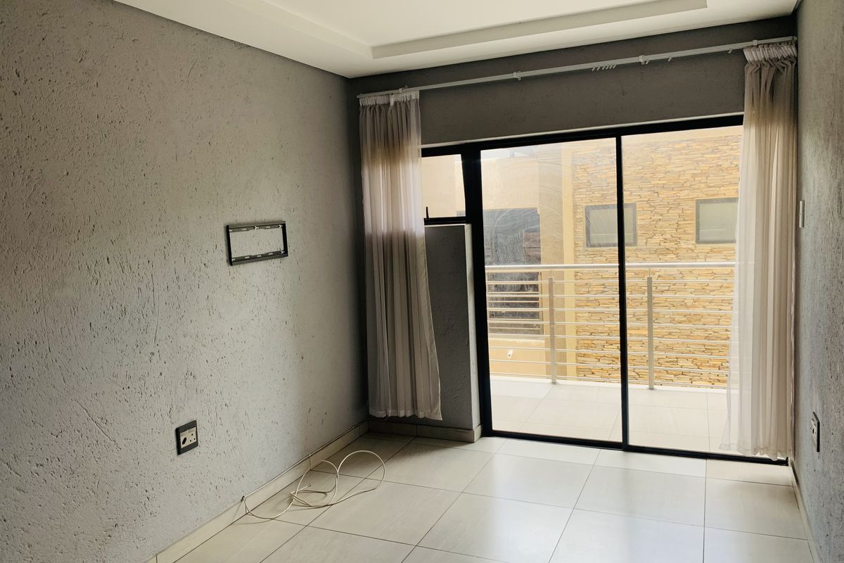 An empty living room featuring tiled floors, a recessed ceiling, and a sliding glass door providing access to a balcony.
