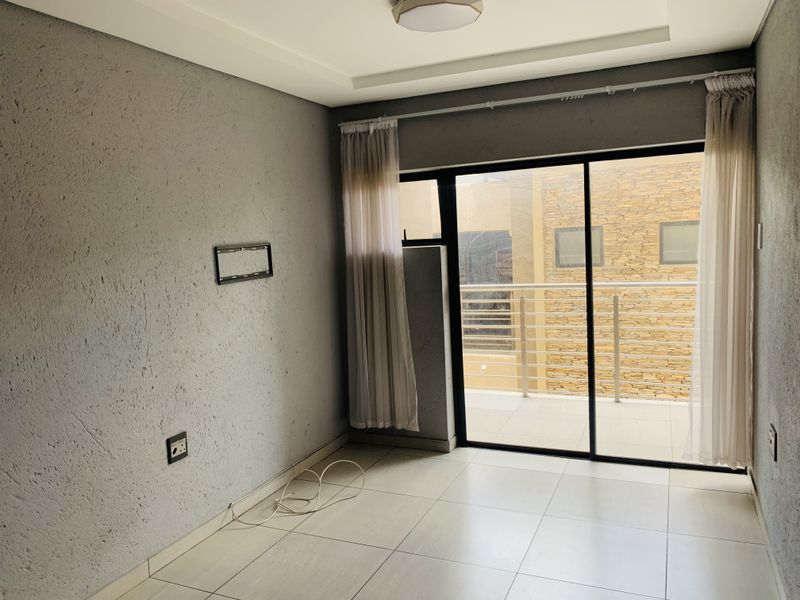An empty living room featuring tiled floors, a recessed ceiling, and a sliding glass door providing access to a balcony.