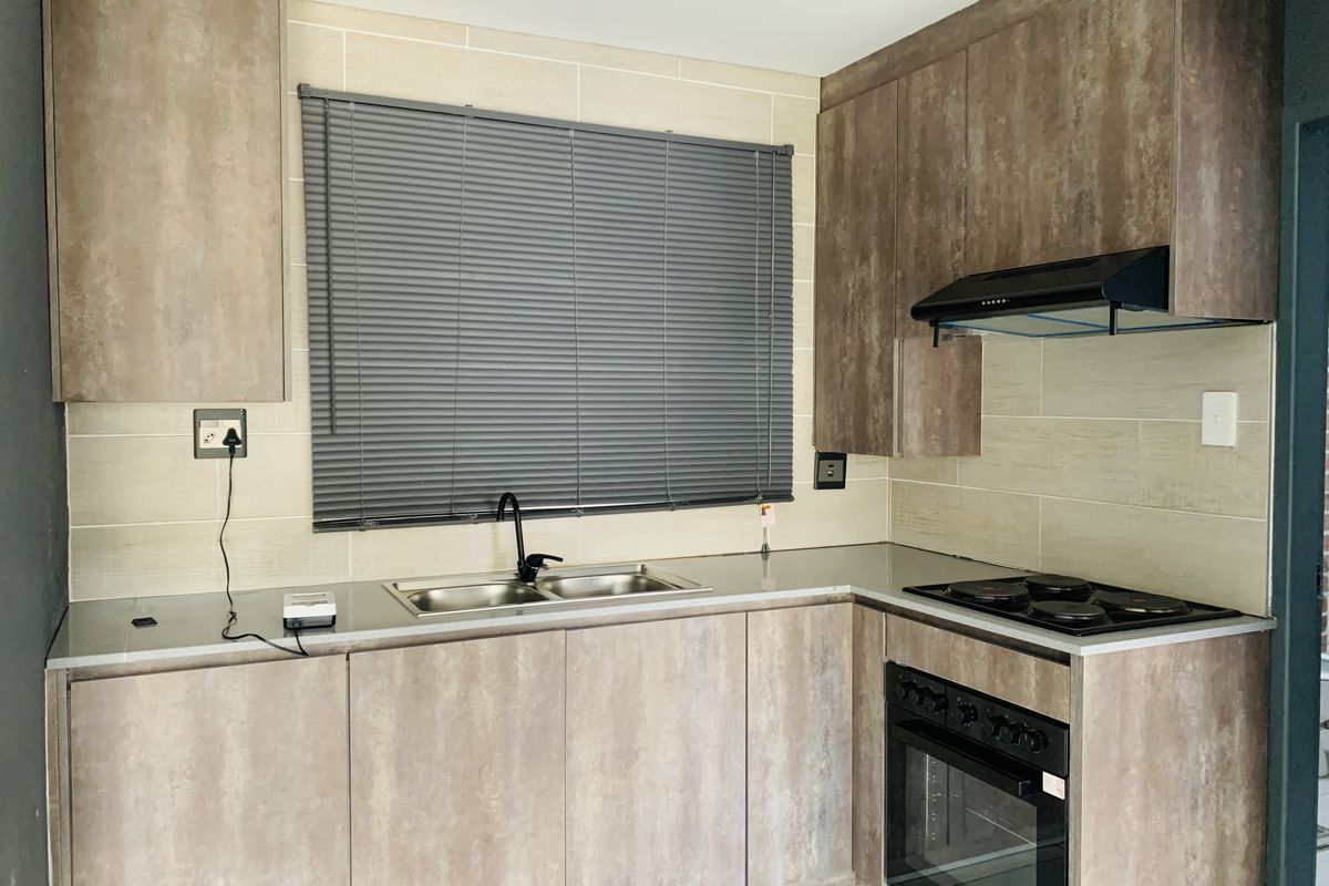 Modern kitchen featuring textured wood-look cabinetry, stainless steel sink, integrated electric oven and hob, and a neutral tiled backsplash.