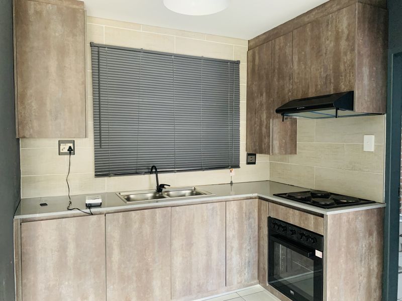 Modern kitchen featuring textured wood-look cabinetry, stainless steel sink, integrated electric oven and hob, and a neutral tiled backsplash.