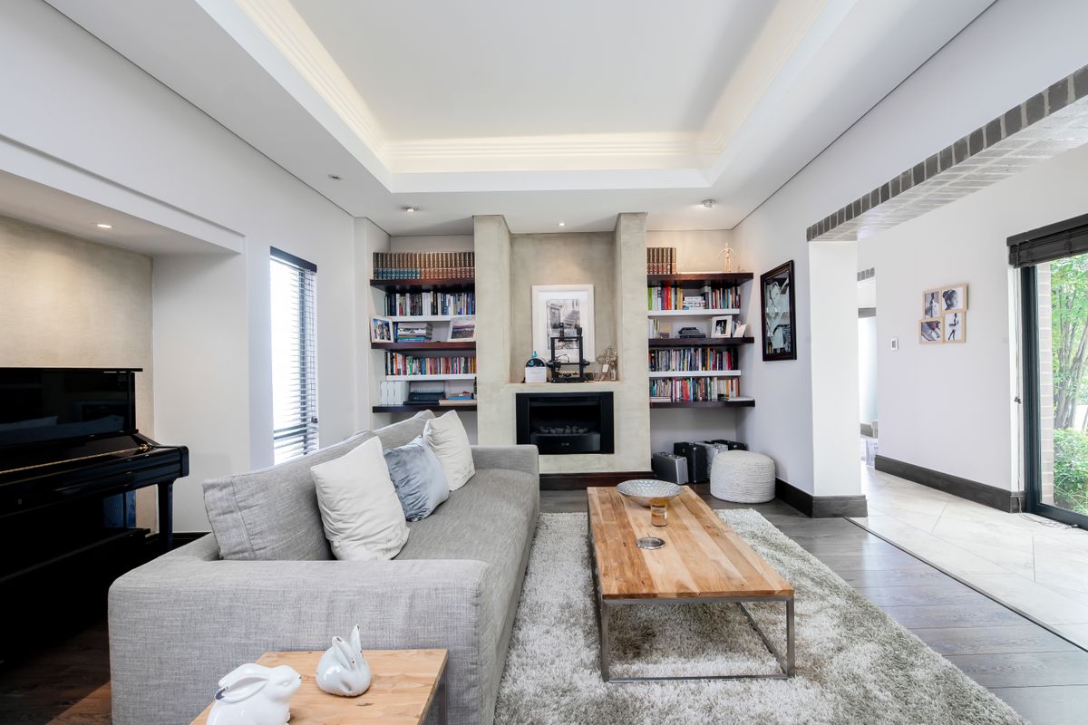 A well-appointed living room featuring a central fireplace, built-in shelving, recessed tray ceiling lighting, and dark timber flooring.