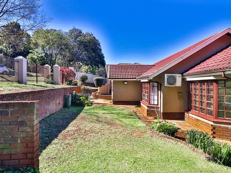 A well-maintained rear exterior view featuring a brick retaining wall, landscaped lawn, paved walkway, and a tiled roof with an external air conditioning unit.