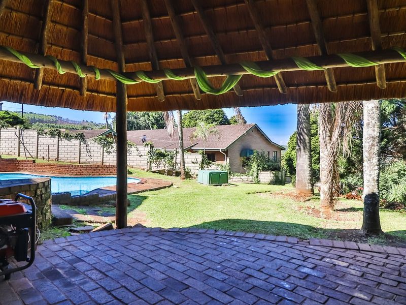 Covered outdoor patio area with a traditional thatch roof, overlooking a private garden and swimming pool.