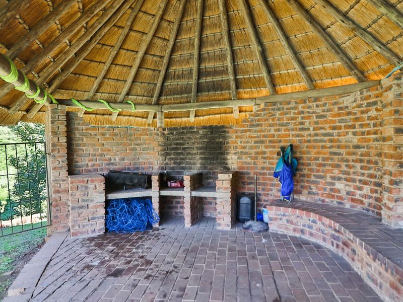 Outdoor thatched lapa area featuring a built-in brick braai, curved brick seating, and paved flooring, ideal for garden entertaining.