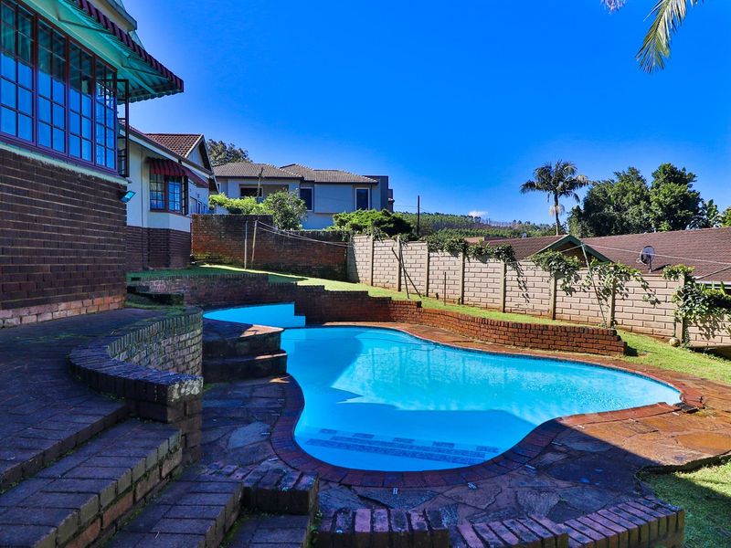 Outdoor pool area featuring a kidney-shaped swimming pool, brick retaining walls, and stone paving, set within a private garden with boundary walling.