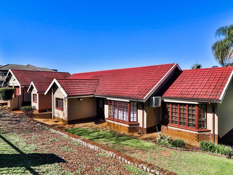 A well-maintained single-story residential property featuring a red tiled roof, brick exterior, and charming bay windows, set within a landscaped garden area.