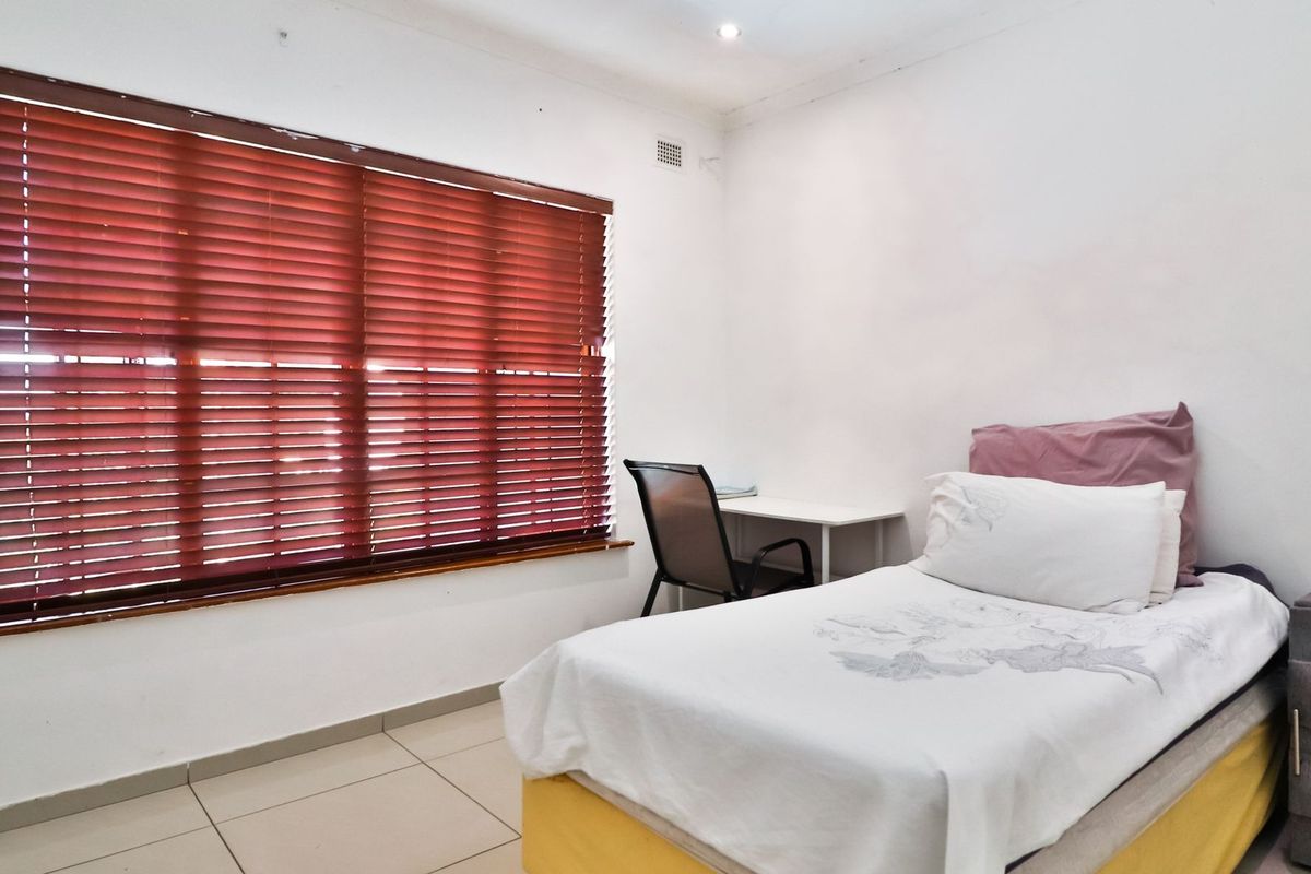 A functional bedroom featuring tiled flooring, recessed downlighting, and large windows fitted with venetian blinds.