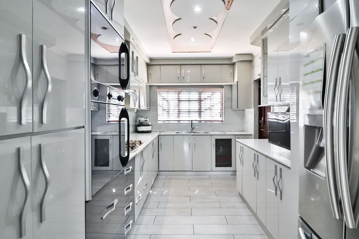 Modern galley-style kitchen featuring high-gloss cabinetry, integrated oven, gas hob, and sleek tiled flooring with recessed ceiling lighting.