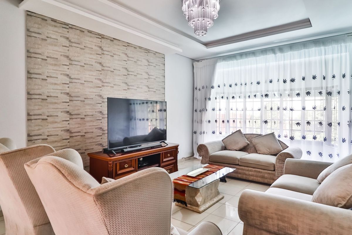 A well-maintained living room featuring a textured accent wall, tiled flooring, and an elegant crystal chandelier, creating a bright and inviting atmosphere.