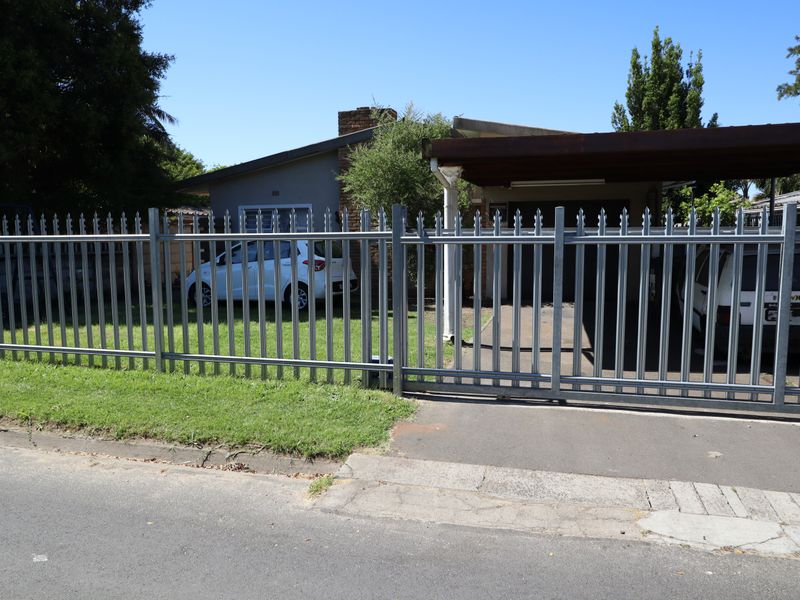Front view of the property featuring a secure steel palisade fence, sliding gate, and a covered carport area.