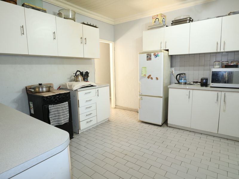 A functional kitchen featuring white cabinetry, tiled flooring, and a tiled backsplash, offering a practical layout with potential for modern updates.