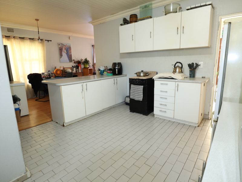 A functional kitchen featuring white cabinetry, laminate countertops, and tiled flooring, offering a dated aesthetic with potential for modern renovation.