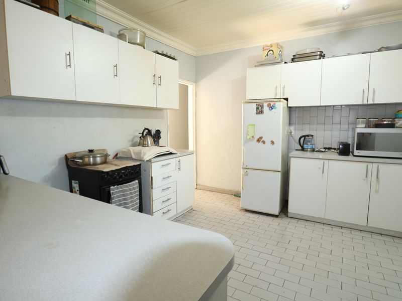 A functional kitchen featuring white built-in cabinetry, tiled backsplash, and tiled flooring, offering a practical layout with potential for modern updates.