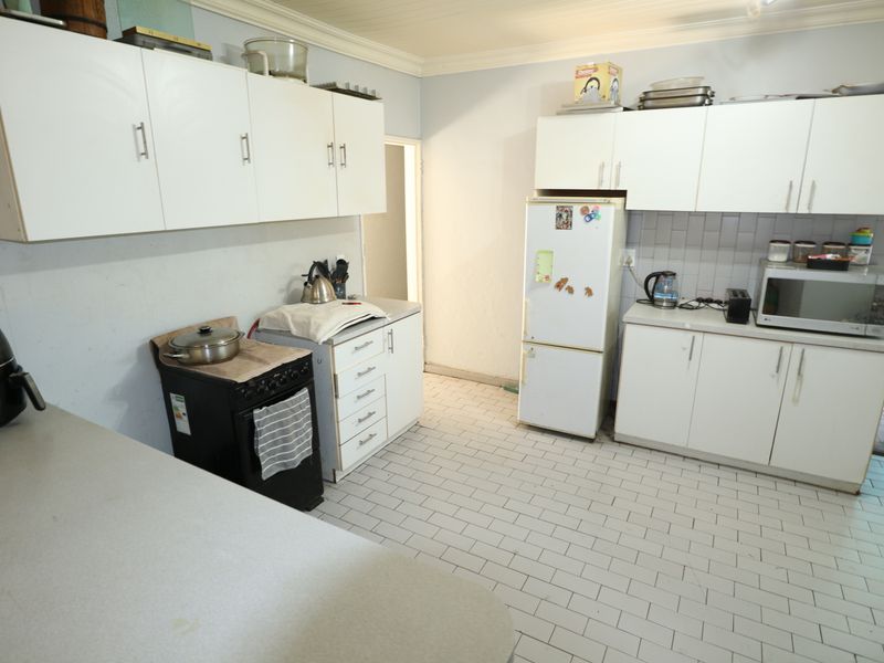A functional kitchen featuring white cabinetry, tiled flooring, and a tiled backsplash, offering a practical layout with ample storage space.